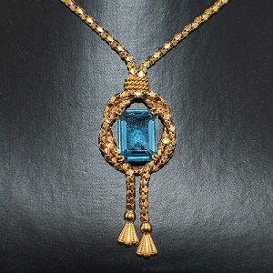 Gargantilla cordon de or amarillo de 18k con una cadena popcorn entrelazado al rededor de una gran espinela azul talla esmeralda, y terminando en borlitas.