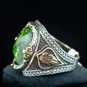 Anillo sello de plata con la peculiar piedra sultanita ovalada facetada enmarcada en cuentas de turquesitas y brazo decorado con la cabeza de un águila imperial y de acabados dorados y plateados.