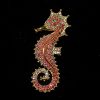 Broche de plata dorada con la forma de un caballito de mar y con decoraciones de circonitas en tonos rojos
